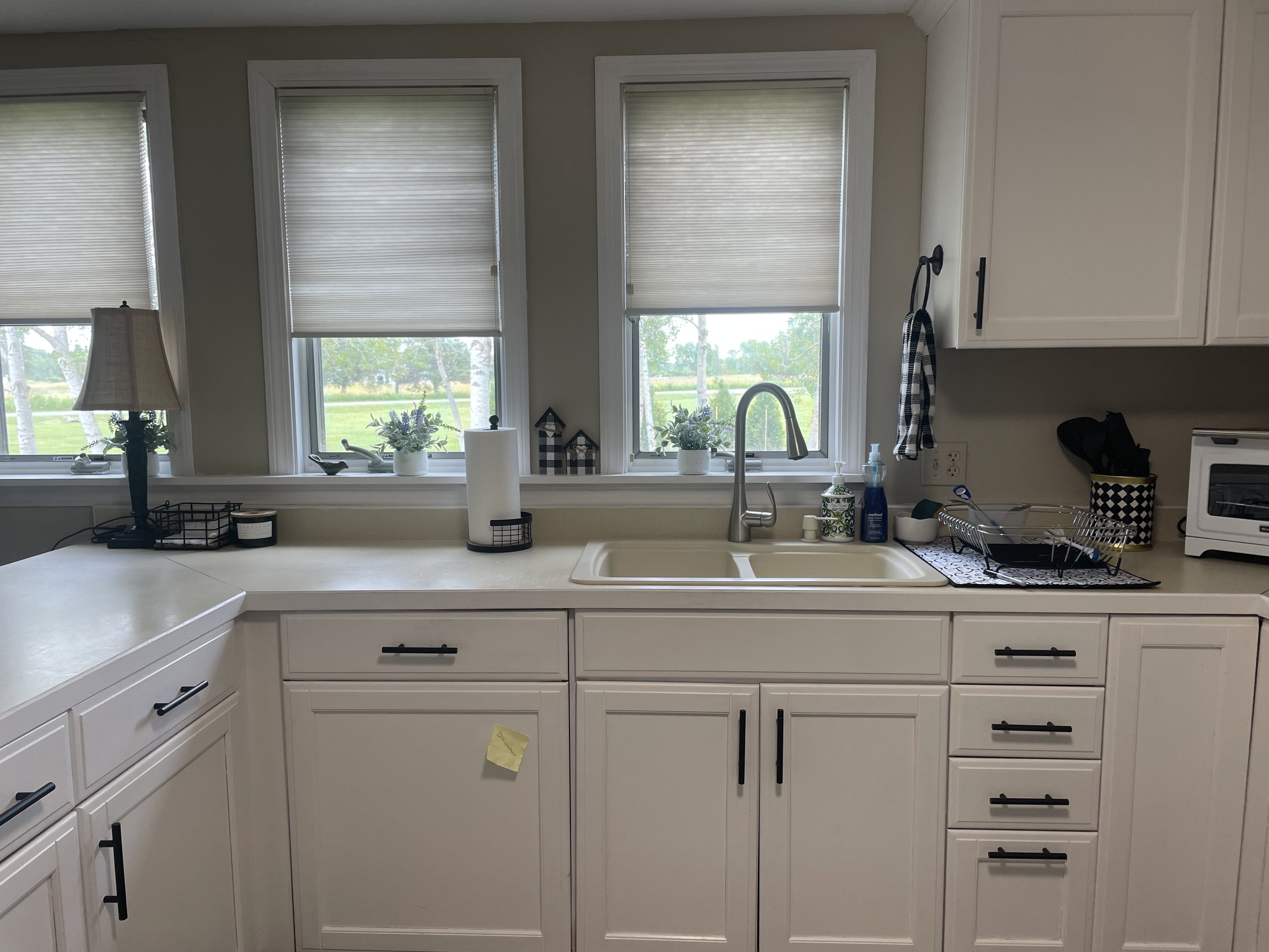 Farmhouse sink beneath three shaded windows overlooking the back lawn