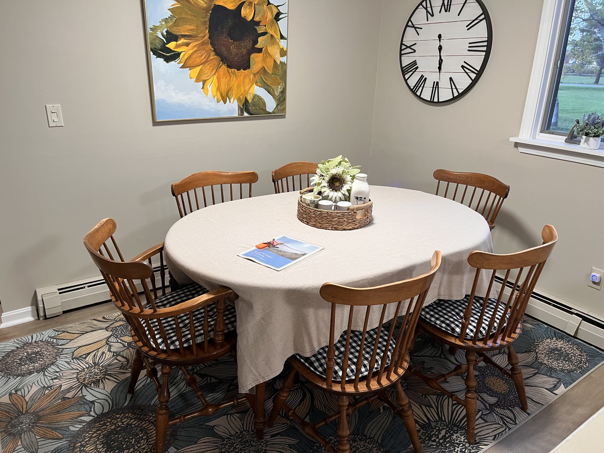 Round dining table set for six beneath a sunflower painting and clock