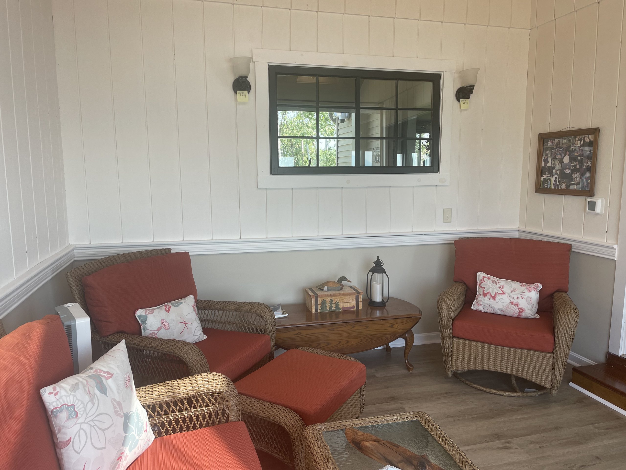 Wicker porch chairs with coral cushions and a wall of family photos