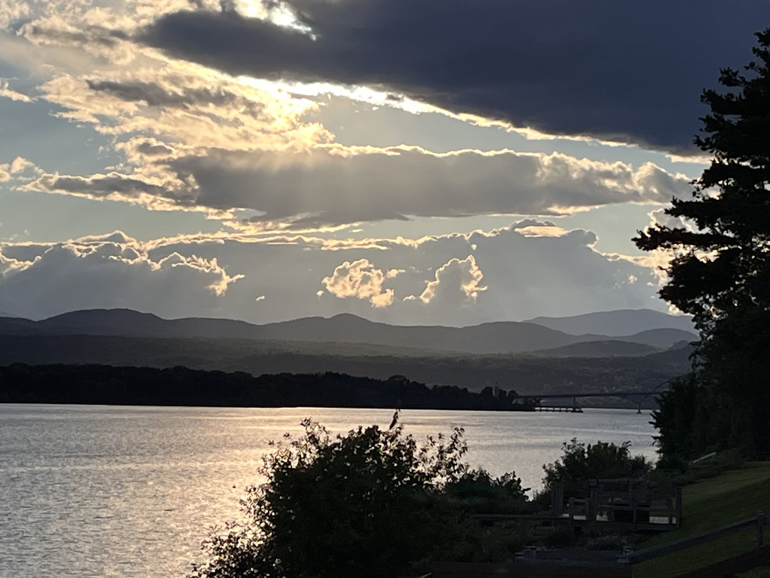 Storm clouds part at dusk, sunlight glinting off the lake near the bridge