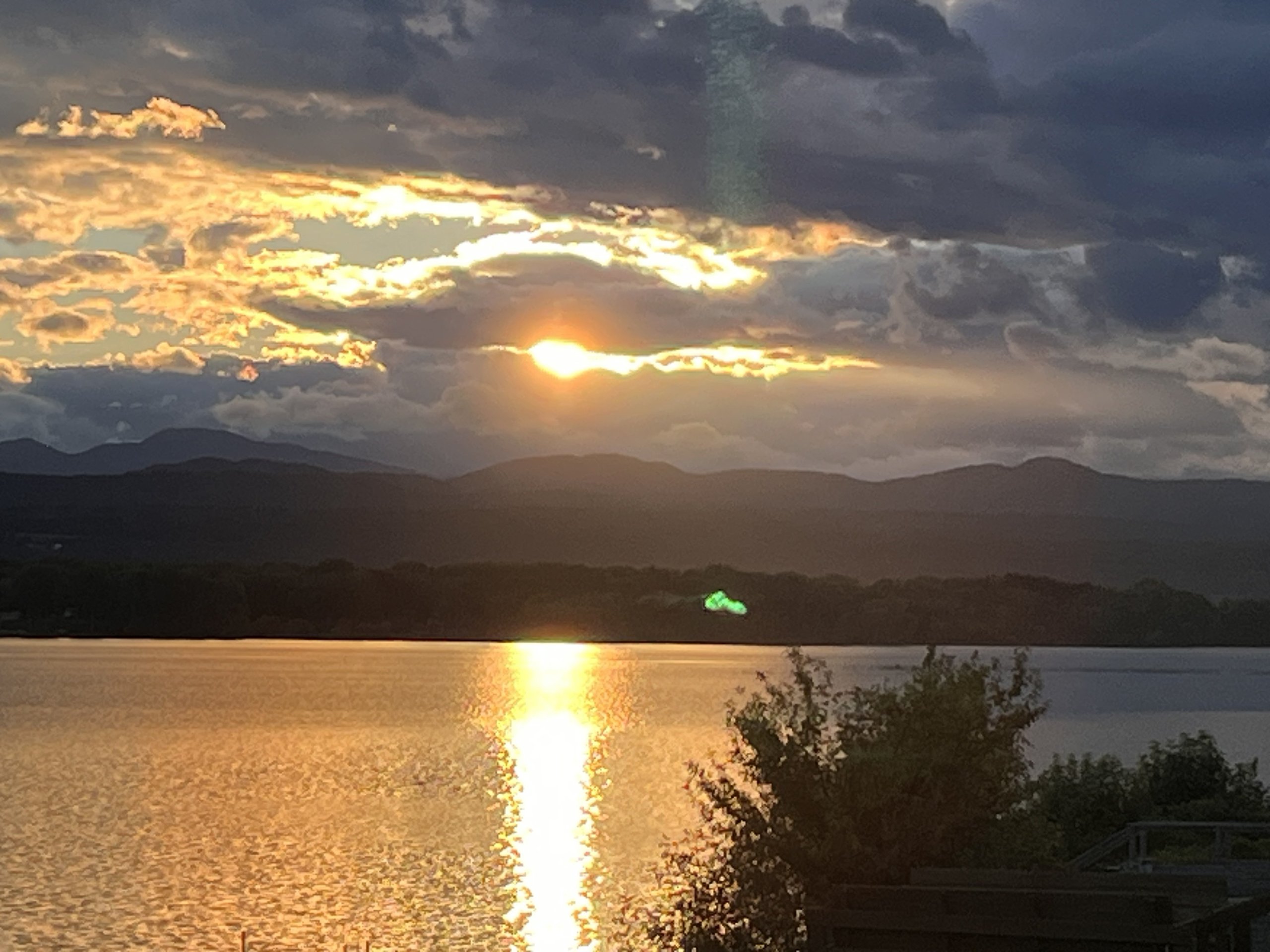 Sunbeams break through storm clouds as the sun sets behind distant mountains