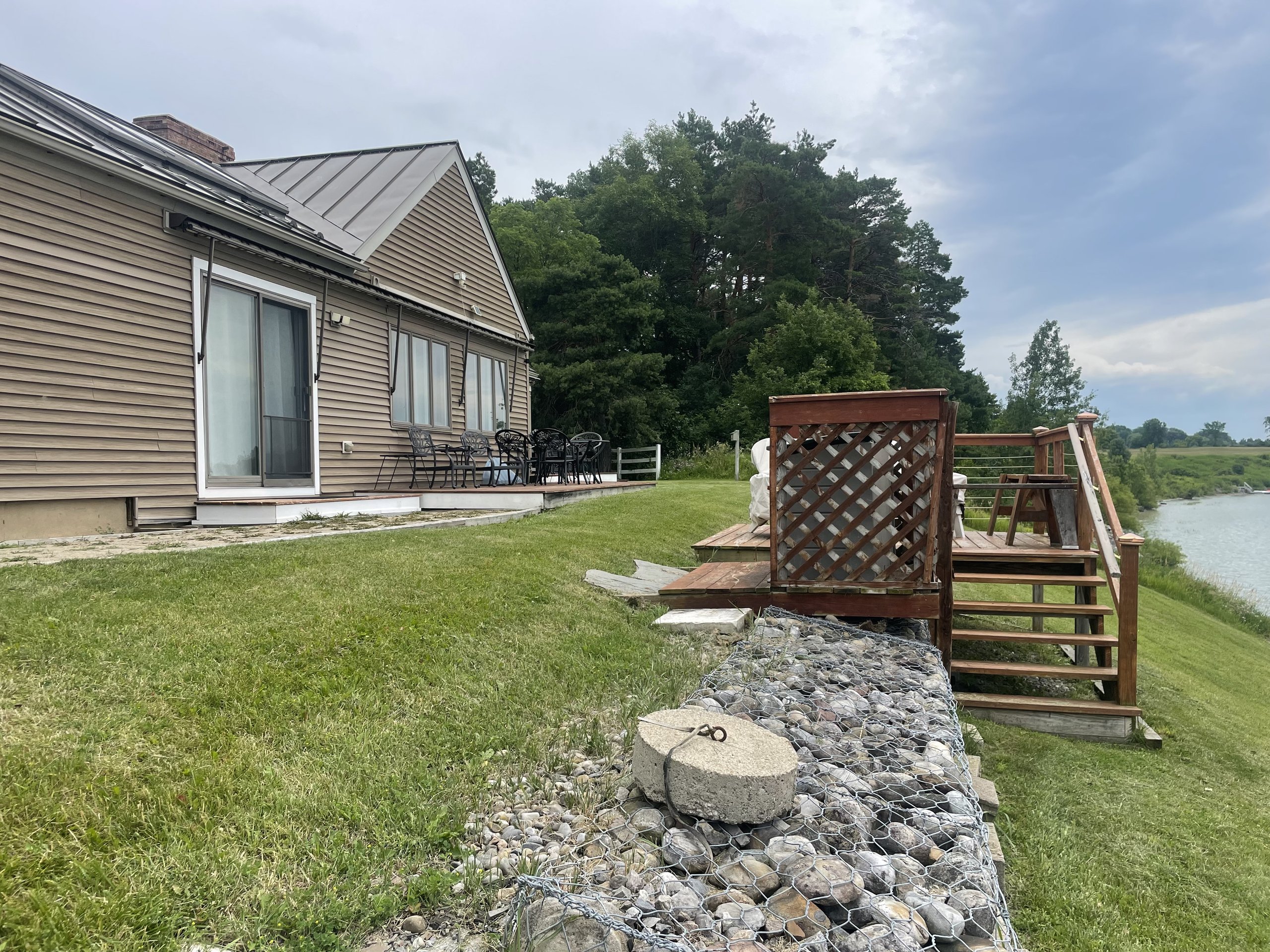 Wide view of the lake house, deck, and shoreline under overcast skies