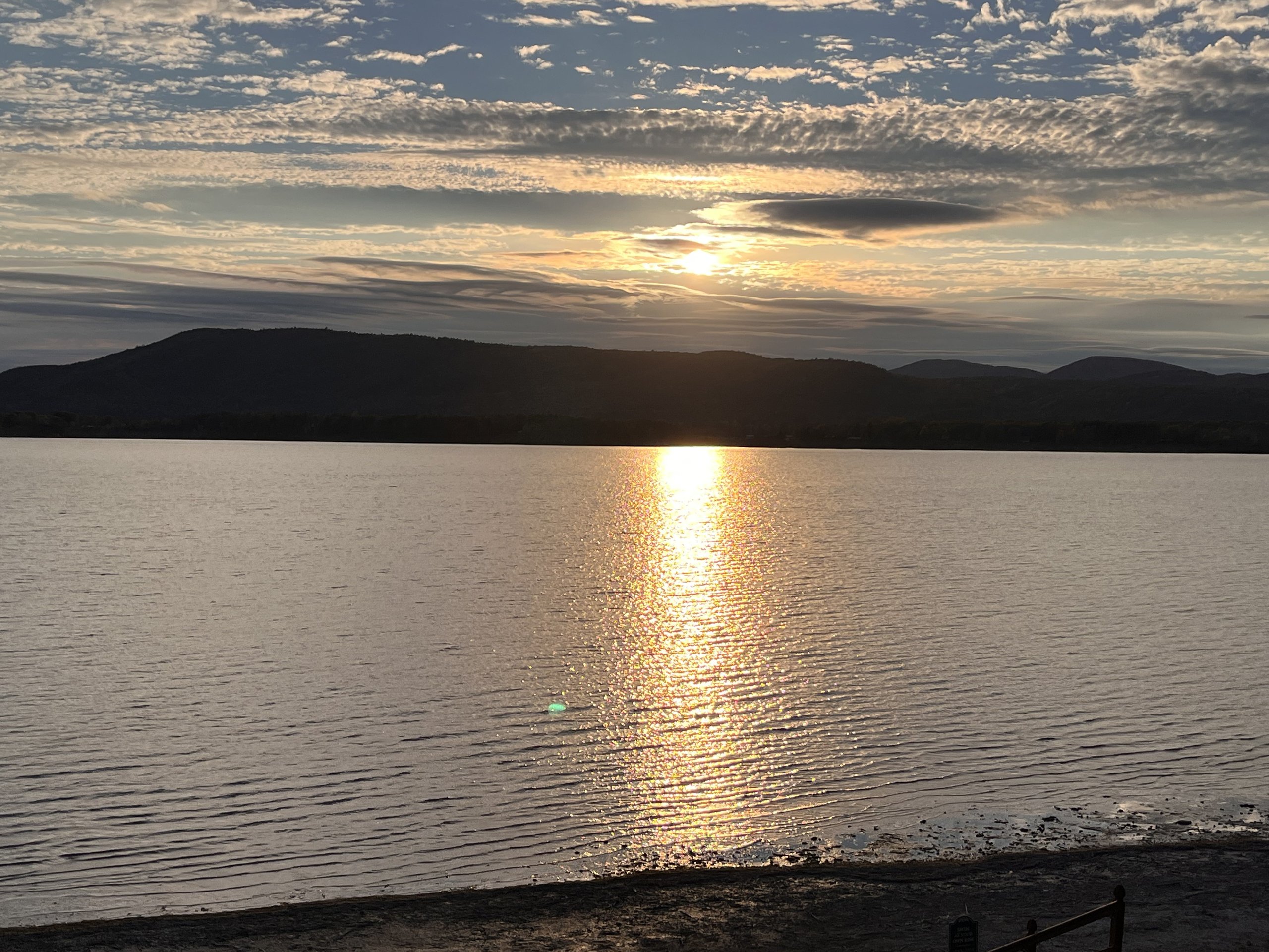 The sun dips toward the mountain ridge, casting a soft glow on the water