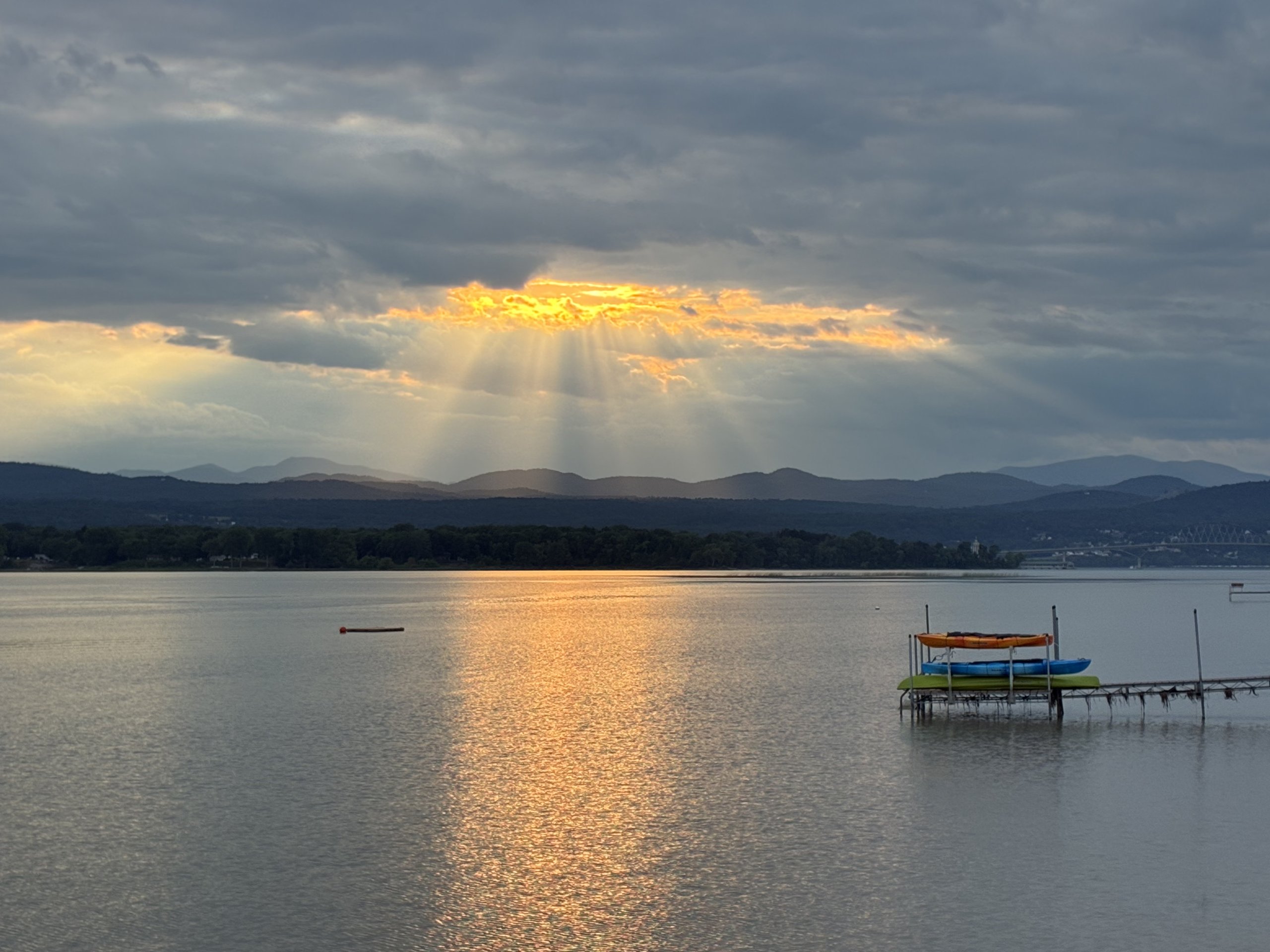 Kayaks and a paddleboard rest on the dock rack under a glowing sunset sky