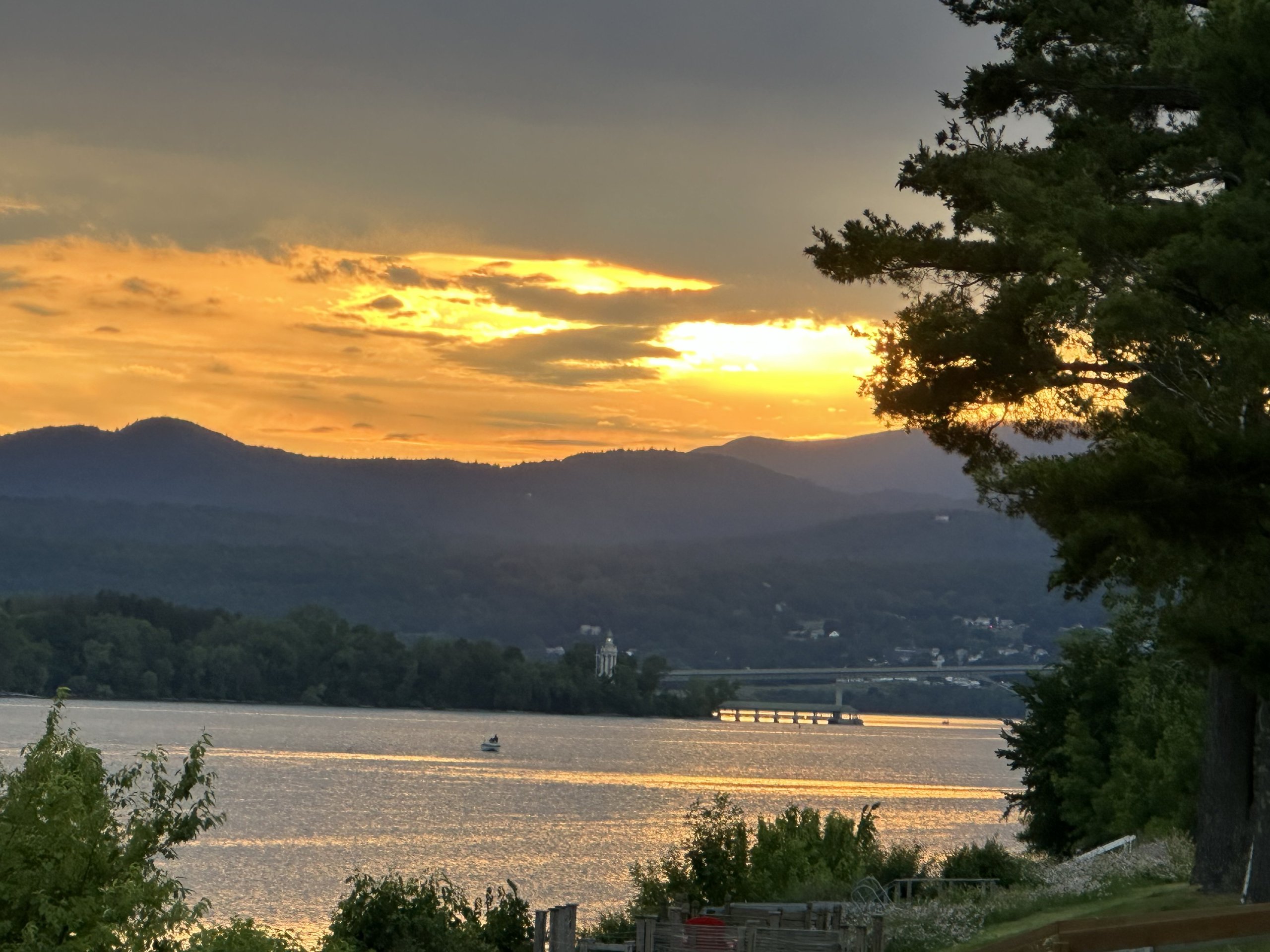 A small boat crosses the lake as sunset colors blaze beyond the bridge