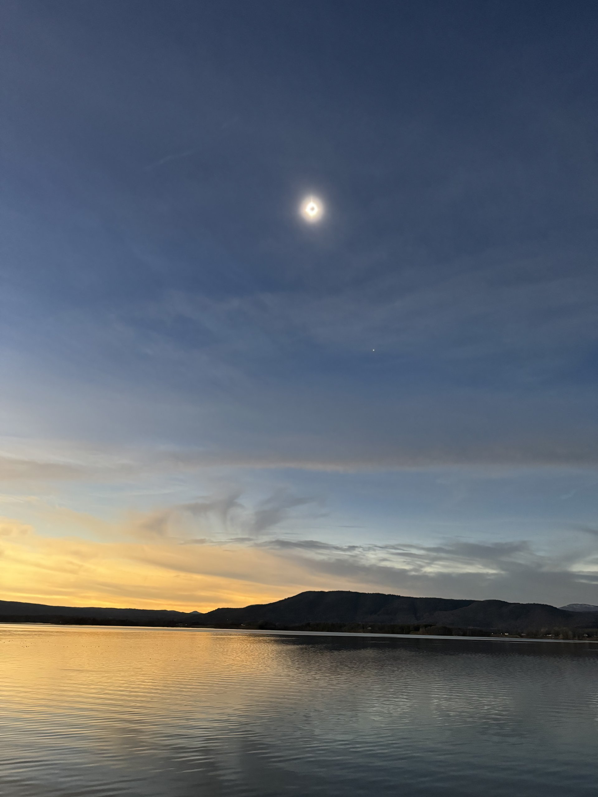 A total solar eclipse glows above the lake during twilight