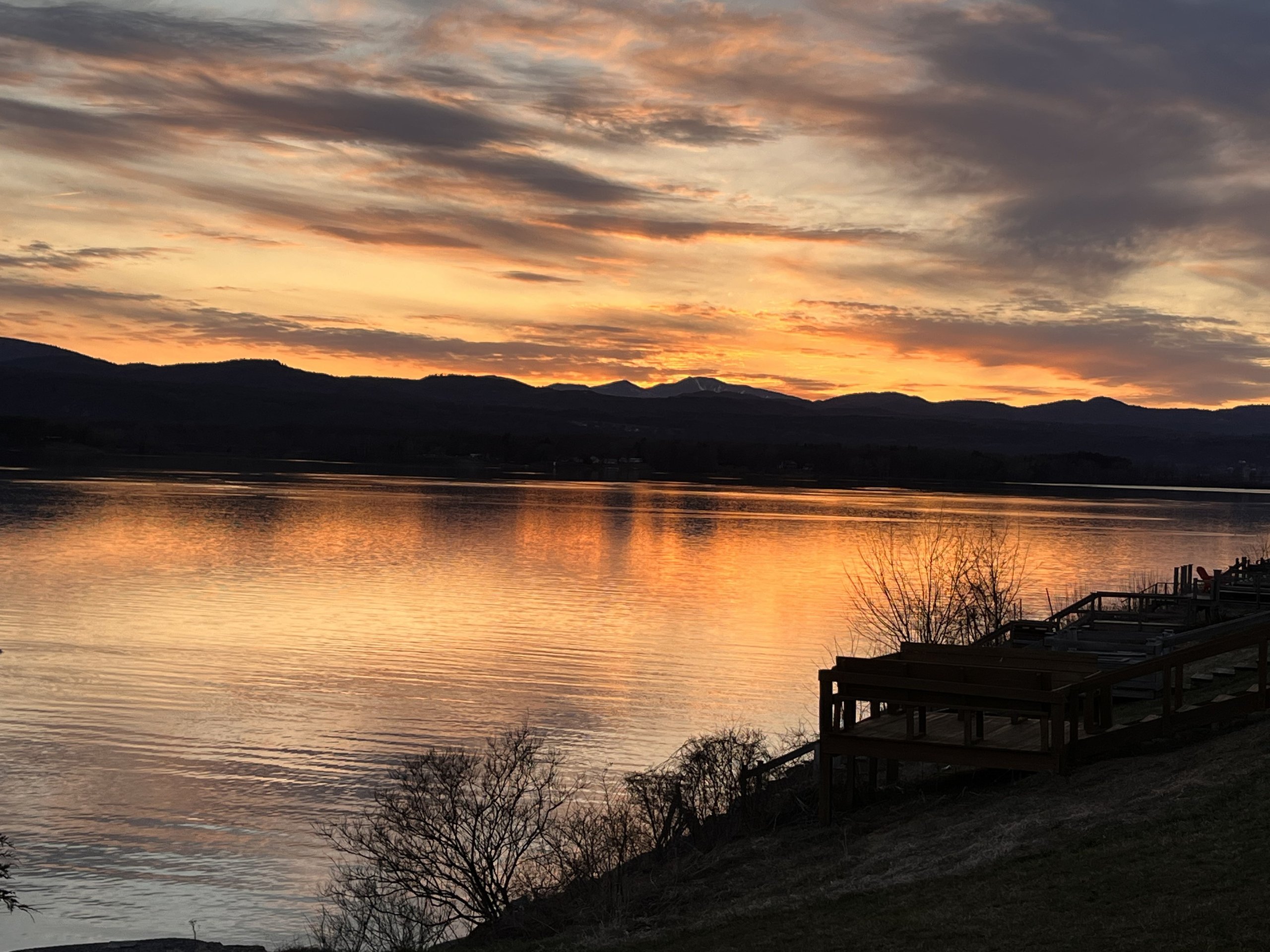 Fiery sunset over Lake Champlain with snow-capped Adirondacks silhouetted beyond the deck