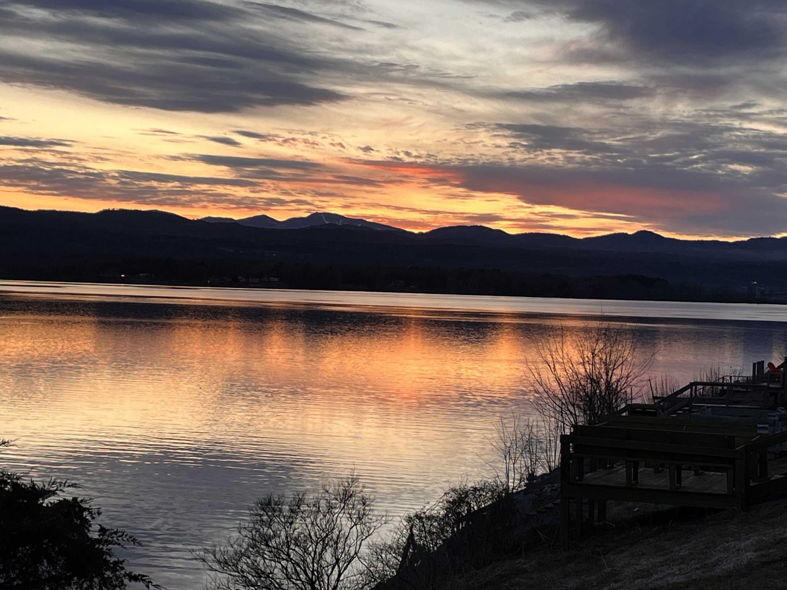 Golden dusk light fades behind snow-dusted Adirondack peaks across the water