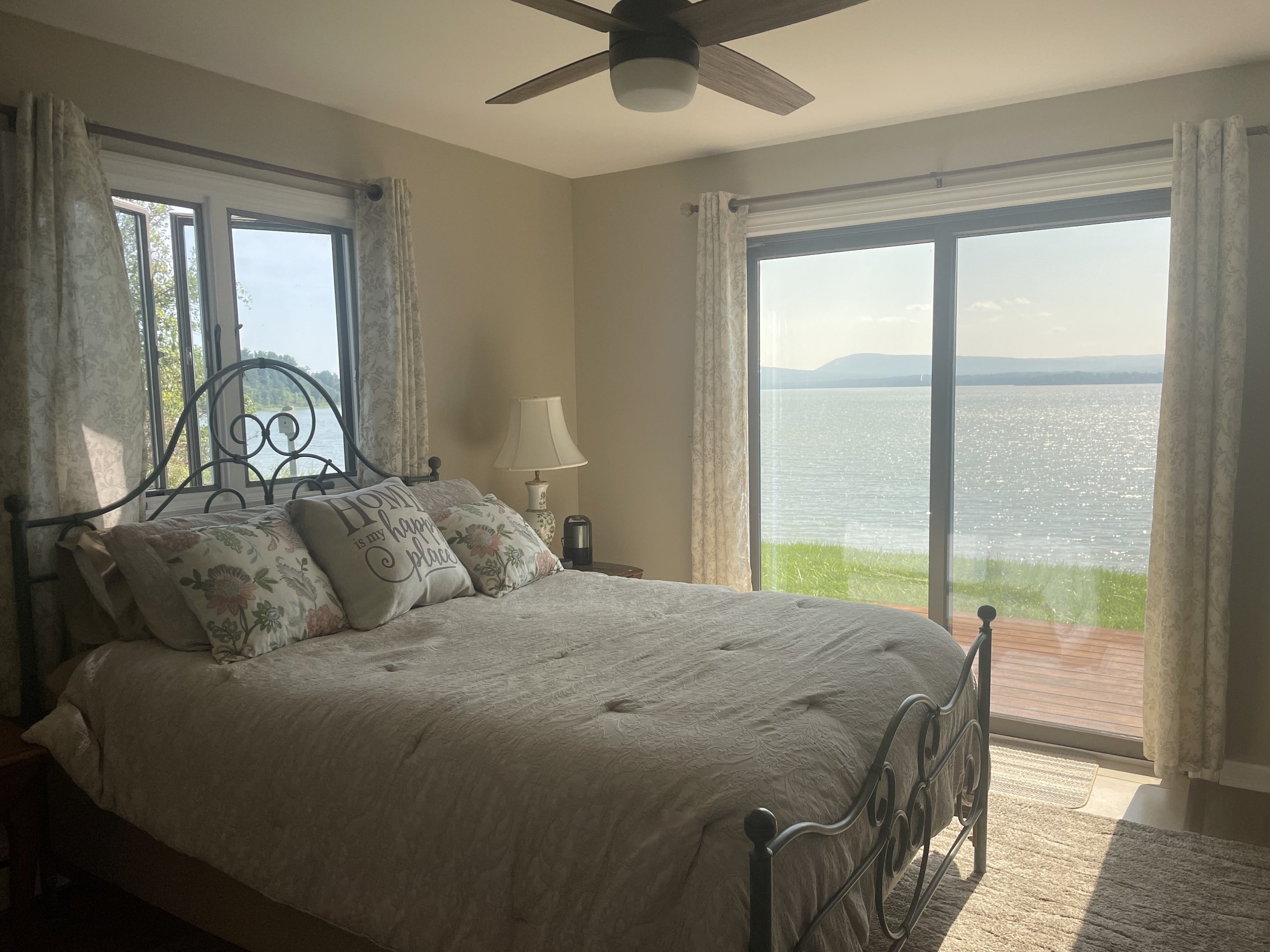 King bed facing a sunlit lake view through sliding glass doors